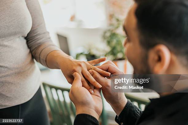 romantic man putting ring on girlfriend's finger at home - verlobung stock-fotos und bilder