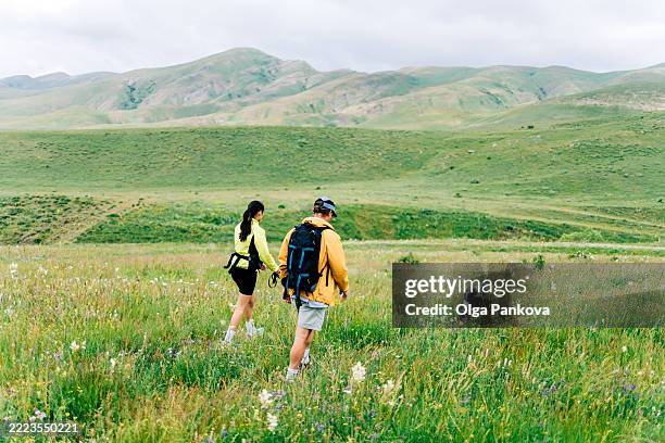 hikers walking through wildflower meadow in mountain valley with dog - dog chasing man stock pictures, royalty-free photos & images