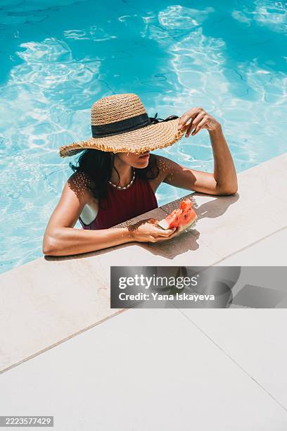unregognizable woman in a straw hat enjoying summer with a slice of fresh watermelon by a poolside - simple living stock pictures, royalty-free photos & images