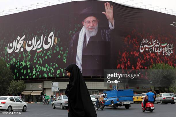 An Iranian crosses a street next to a billboard bearing the portrait of Iranian supreme leader Ayatollah Ali Khamenei and a quote reads in Persian...