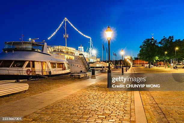 stockholm embankment illuminates at dusk with docked ships - empty street stockfoto's en -beelden