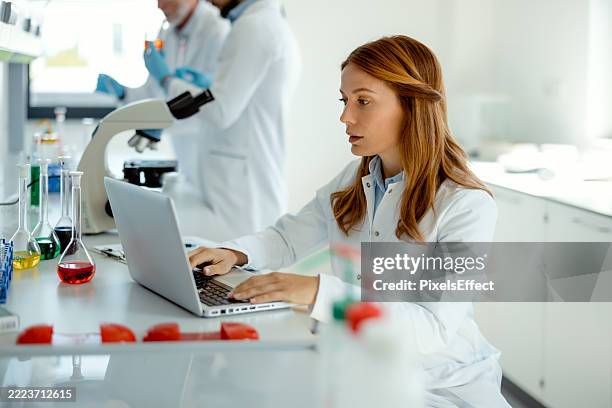 woman researcher analyzing data on laptop in lab - biochemie stockfoto's en -beelden