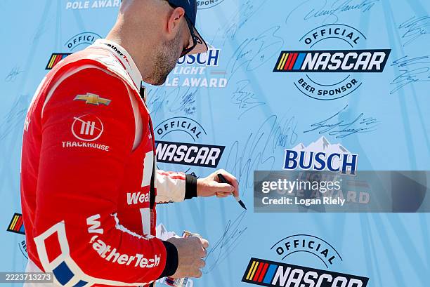 Shane Van Gisbergen, driver of the WeatherTech Chevrolet, signs the Busch Light Pole Award backdrop after winning the pole award during qualifying...