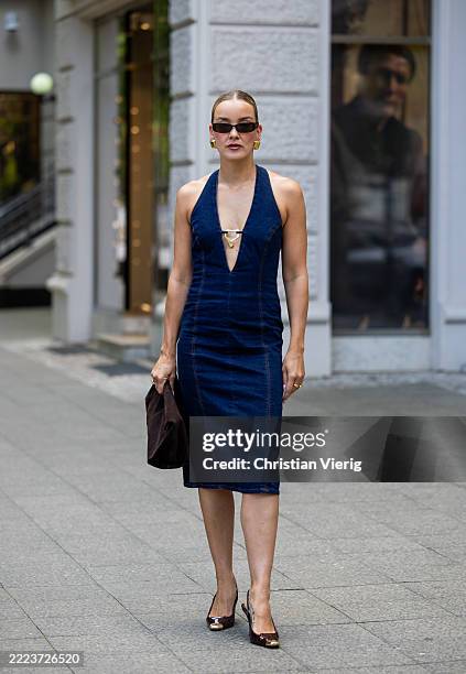 Tina Haase wears Meshki denim jeans dress, flattered brown suede clutch bag, metal toe brown pumps, Corlene brown sunglasses on July 05, 2025 in...