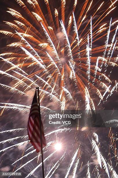 Fireworks light up the night sky as a national flag of the United States flutters at a park to celebrate Independence Day on July 4, 2025 in City of...