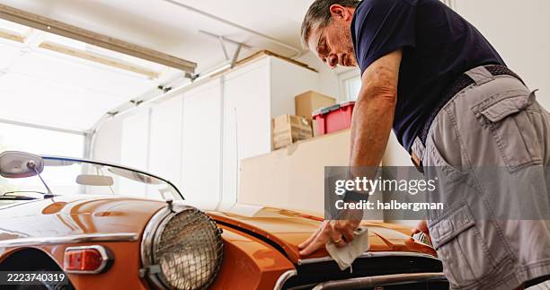 senior man holding down the bonnet of his vintage convertible car inside garage - klassieke auto stockfoto's en -beelden