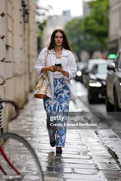 Guest wears a white oversized button-up shirt with long sleeves, layered over a white ribbed tank top. The pants feature a blue and white floral...