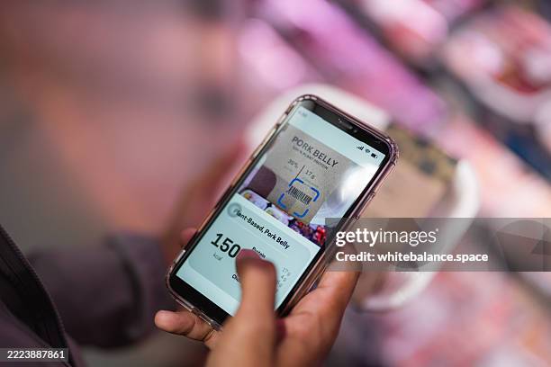 close-up shot of a man using his smartphone to check his smart fridge while grocery shopping at the supermarket - buy online pick up in store stock pictures, royalty-free photos & images