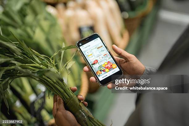 close-up shot of a man using his smartphone to check his smart fridge while grocery shopping at the supermarket - buy online pick up in store stock pictures, royalty-free photos & images