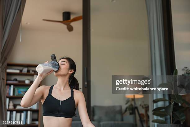 junge frau in sportbekleidung sitzt auf einer yogamatte und trinkt molkenprotein nach ihrer praxis zu hause - molke stock-fotos und bilder