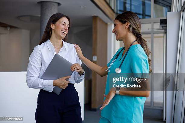 doctor supporting businesswoman with laptop, offering reassurance and empathy in a hospital corridor, fostering trust and care - public service stock pictures, royalty-free photos & images