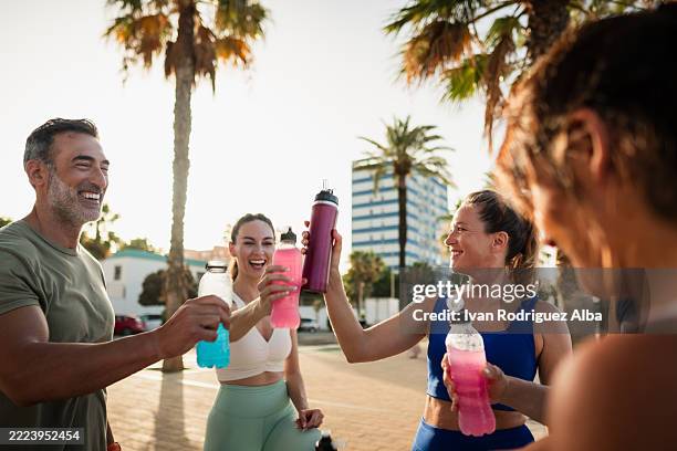 gruppe glücklicher athleten, die nach dem training mit sportgetränken anstoßen - energydrink stock-fotos und bilder