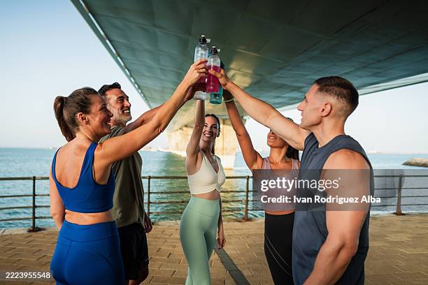 fitnessgruppe stößt nach dem training am meer mit sportgetränken an - energydrink stock-fotos und bilder
