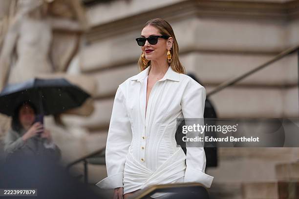 Chiara Ferragni wears a white long-sleeve wrap shirt dress with a collared neckline and gold buttons down the front. The dress features a ruched...