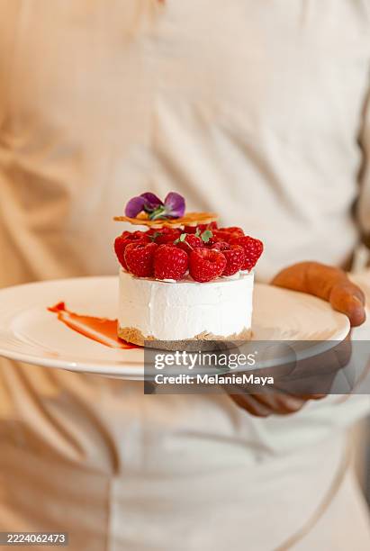 waiter serving elegant cheesecake cake pastry with raspberry served in luxury hotel restaurant - raspberry sauce stock pictures, royalty-free photos & images