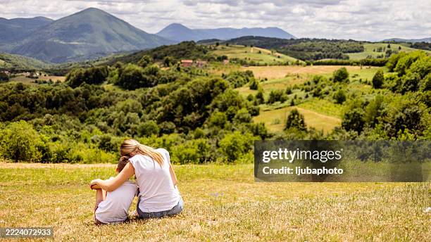 mutter und kind entspannen sich auf einem ruhigen hügel mit panoramablick auf die berge - land in sicht stock-fotos und bilder
