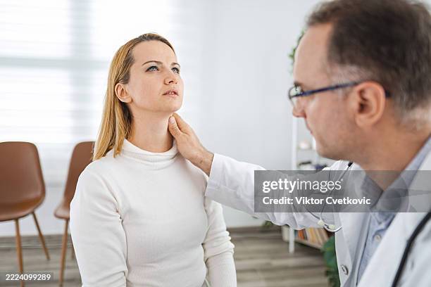 doctor examining patient's neck in medical office - thyroid cancer stock pictures, royalty-free photos & images
