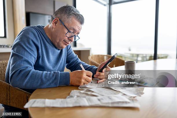 retired man using his cell phone while paying bills at home - struggle stock pictures, royalty-free photos & images