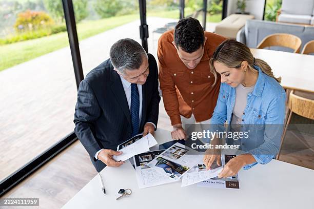 pareja mirando los planos de una casa y haciendo preguntas al agente inmobiliario - agente inmobiliario fotografías e imágenes de stock