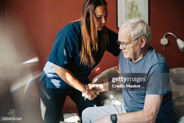 female caregiver helping senior man in getting up from bed in bedroom at retirement home - nursing assistant stock pictures, royalty-free photos & images