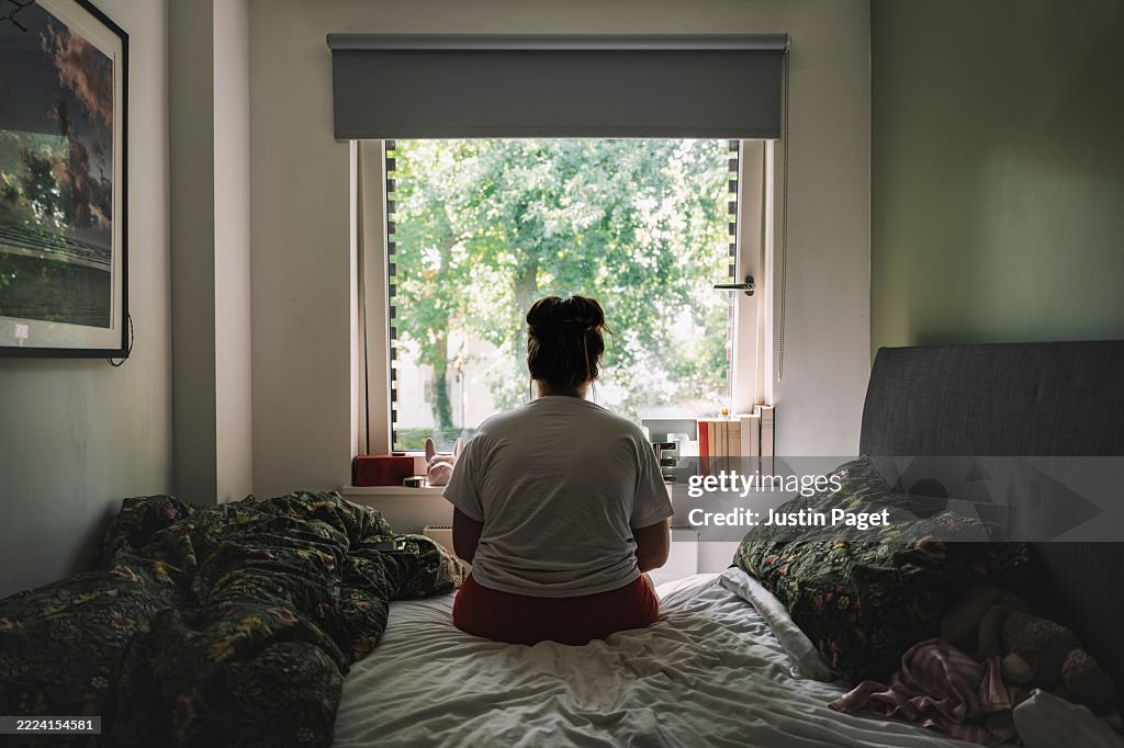 Rear view of a young woman looking out of the window - negative emotion