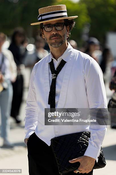 Ulisses de Melo wears a straw boater hat with black ribbon, black rectangular glasses, a white shirt under a white waistcoat with a black textured...