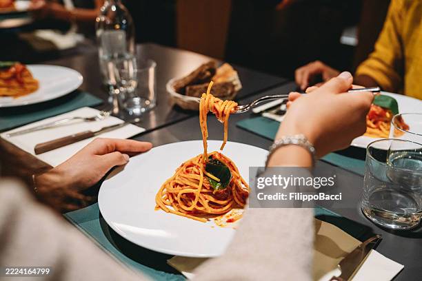 woman eating spaghetti with tomato sauce and basil in a restaurant - pasta stock pictures, royalty-free photos & images