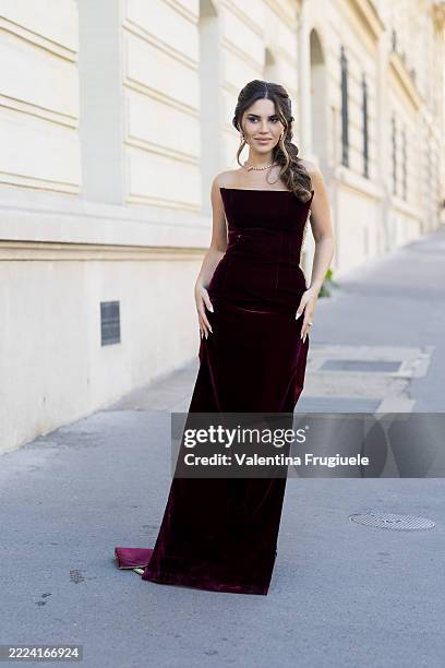 Nojoud Alrumaihi wears a strapless burgundy velvet gown with a fitted bodice and floor-length hem, styled with a pearl choker necklace and side-swept...