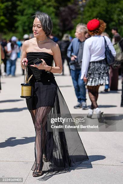 Guest wears a strapless black dress featuring a textured bodice and a sheer overlay skirt. The hair is styled in a short, sleek bob with a gray hue....