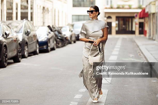 Gili Biegun wears silver light blue silk maxi dress with over the shoulder cape, white slingback kitten heels shoes, white shoulder bag, black...