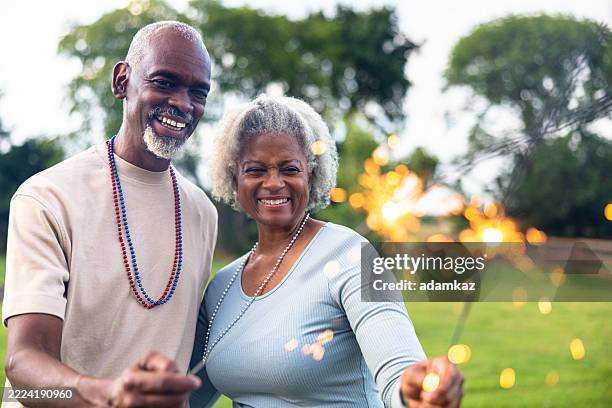 pareja negra patriótica estadounidense de la tercera edad que celebra el 4 de julio con bengalas y decoraciones - historia negra de estados unidos fotografías e imágenes de stock