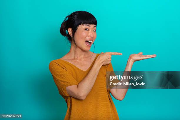 femme joyeuse pointant le placement de produit sur un fond turquoise - gestes photos et images de collection