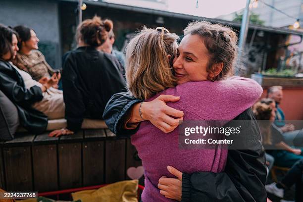 friends embracing in a cozy outdoor setting during a social gathering - omhelzen stockfoto's en -beelden