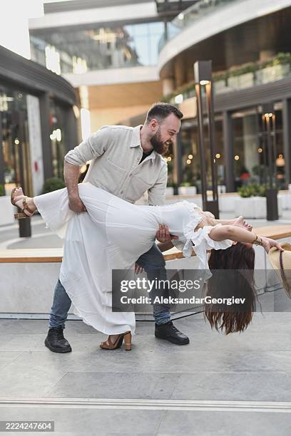 femmina romantica che si appoggia all'indietro tra le braccia del partner mentre ballano liberamente in piazza urbana - piegarsi allindietro foto e immagini stock