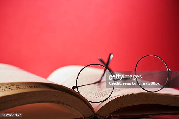 round reading glasses rest on opem page book against red background,malaysia - dizionario foto e immagini stock
