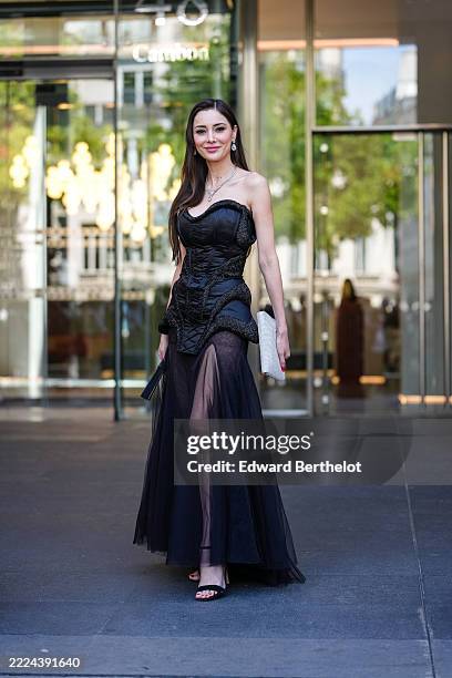 Deborah Valdez-Hung wears a strapless black corset top featuring intricate stitching and textured embellishments. The corset is paired with a sheer...