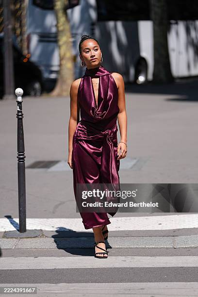 Guest wears a sleeveless, deep burgundy satin dress featuring a halter neckline and a draped bodice. The dress includes a wrap detail at the waist,...