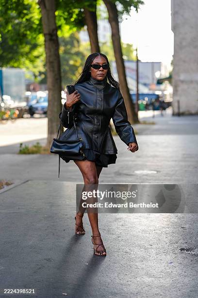 Guest wears a black leather jacket with a high collar and structured shoulders. The jacket features a fitted waist and flares slightly at the hips....