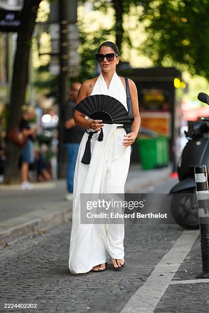 Gili Biegun wears a sleeveless white dress with a halter neckline, featuring a flowing silhouette and black tassel details at the waist. The outfit...