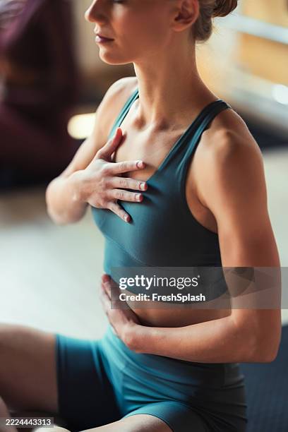 frau, die yoga-meditation in innenräumen mit händen auf herz und bauch übt - einatmen stock-fotos und bilder