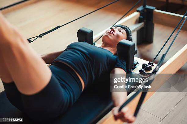 donna che si esercita sulla macchina del reformer di pilates al chiuso in un impianto sportivo - metodo pilates foto e immagini stock