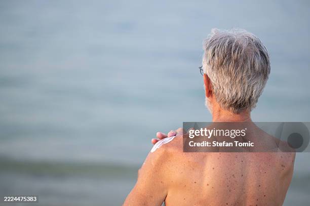 senior man applying sunscreen at the beach on a calm summer day - sun safety stock pictures, royalty-free photos & images