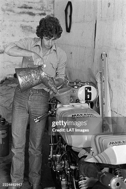 In the garage area, Steve Parrish pours fuel into his Suzuki RG500's tank using a pitcher and a funnel ahead of the German Motorcycle Grand Prix at...