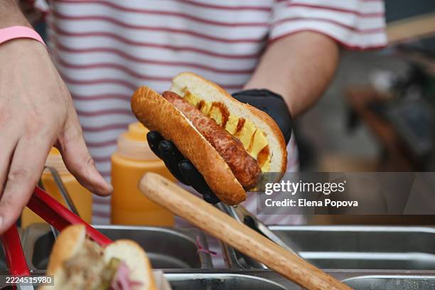 chef's hands making hot dog with sausage, red onion, pickles and mustard sauce at the outdoors concession stand - puesto-de-comida-rápida fotografías e imágenes de stock