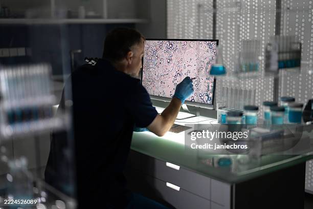 male scientist researcher working in a futuristic medical laboratory. observing magnified pictures of cells on computer screen - pandemia doença imagens e fotografias de stock