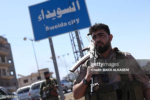 Member of Syria's security forces stands under a sign in the predominantly Druze city of Sweida on July 15 following clashes between Bedouin tribes...