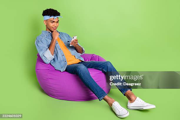 Photo of guy sit beanbag hold phone finger chin wear headband denim shirt footwear isolated green color background
