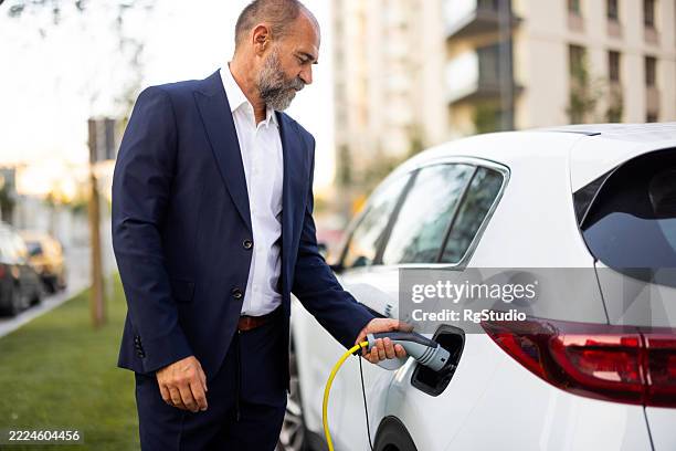 businessman charging electric car in the city - hybrid car stock pictures, royalty-free photos & images