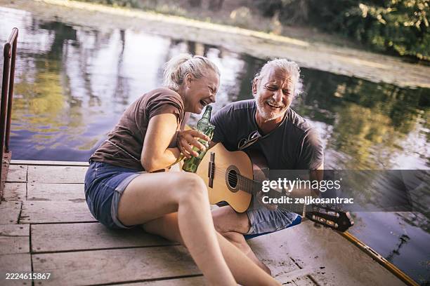 elderly friends sharing joy and music on a lakeside dock at sunset - recreational boat stock pictures, royalty-free photos & images