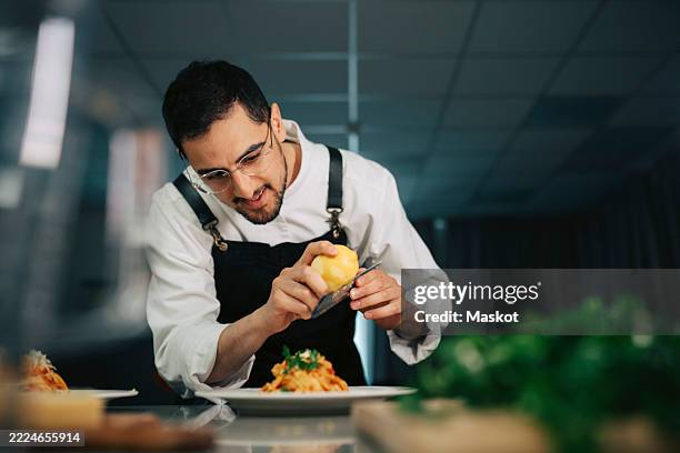 male chef grating lemon zest on tagliatelle pasta while finishing dish in kitchen at restaurant - restauration photos et images de collection